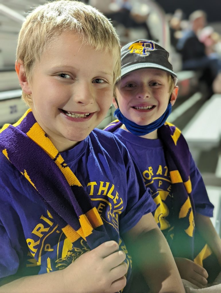 Two smiling boys look at the camera. They are both wearing t-shirts and other sports gear for the Pieper Warriors team in Comal ISD.